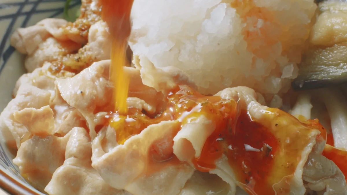 豚肉にソースをかけた料理のクローズアップ写真。大根おろしとナスも添えられている。