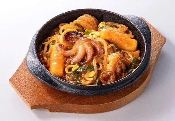 タコと野菜が入った料理が、木製の台座の上に置かれた黒い器に入っています。