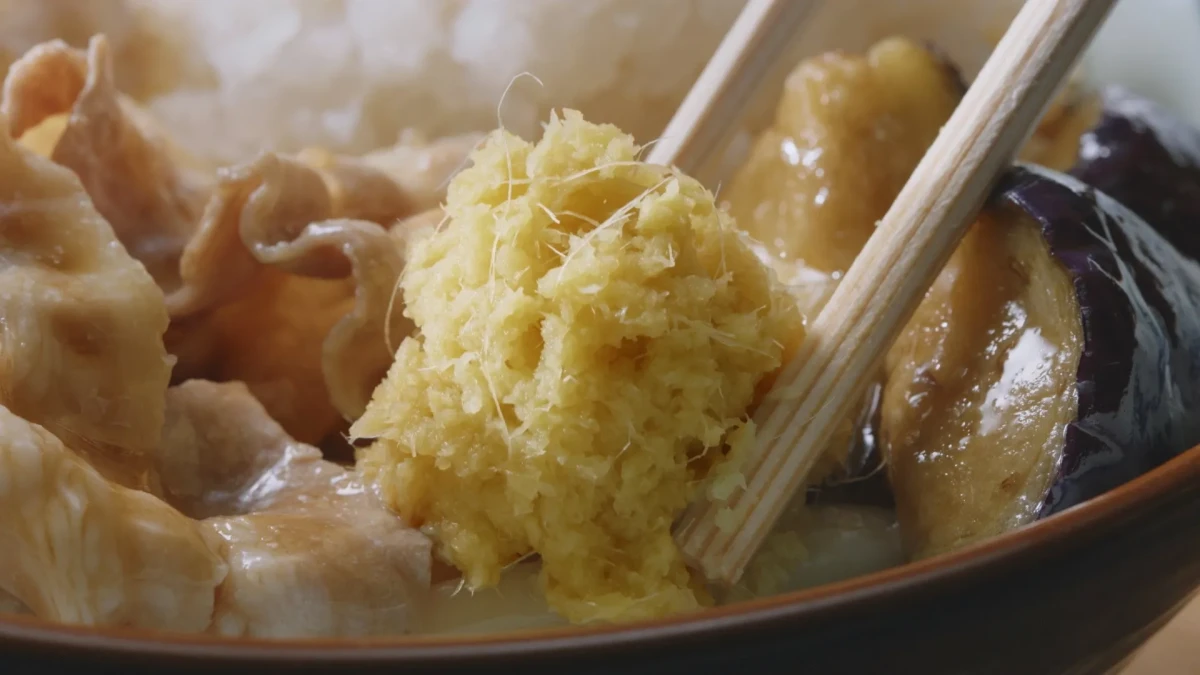お椀に入った料理の写真です。生姜やナスなどの食材が写っています。箸で生姜を掴もうとしている様子です。